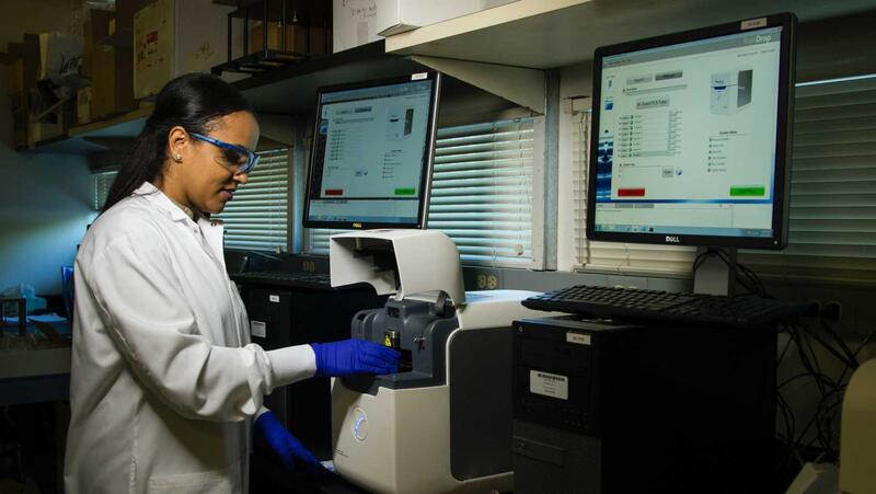Kvinna står i ett laboratorium med rock och handskar på sig