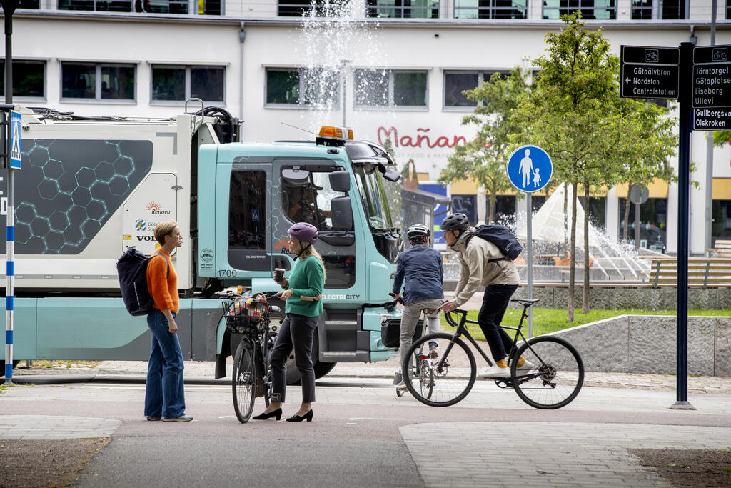 urban miljö, folk står och pratar bland cyklister och lastbilar 